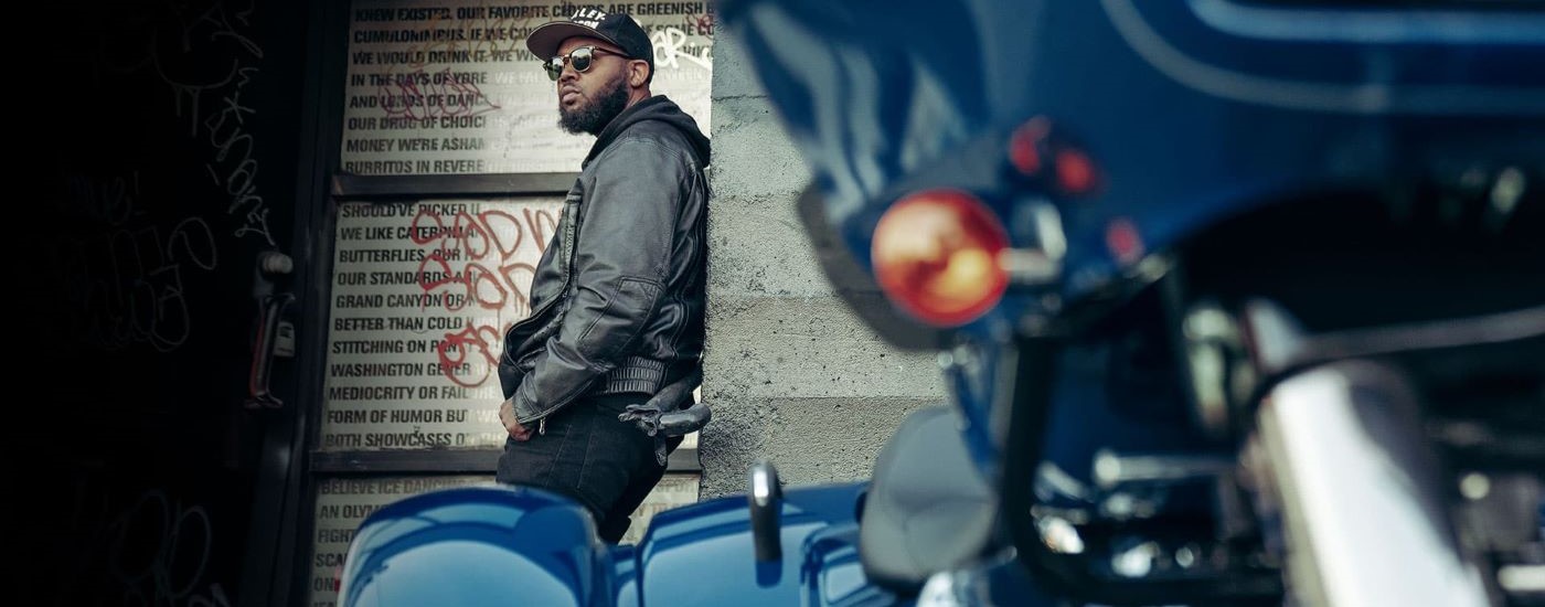 A person is shown leaning against a wall near a blue 2023 Harley-Davidson Road Glide 3