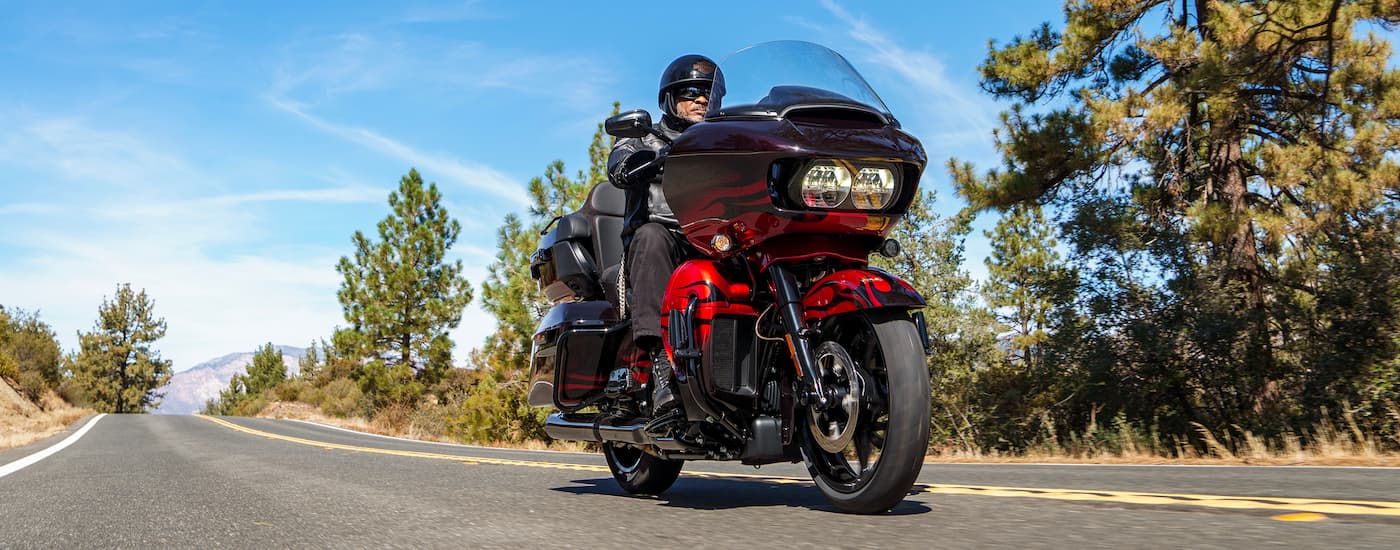 A man is shown riding a red 2022 Harley-Davidson CVO Road Glide Limited on an open road.